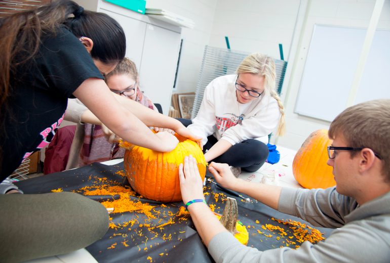 students collaborating on a single pumpkin